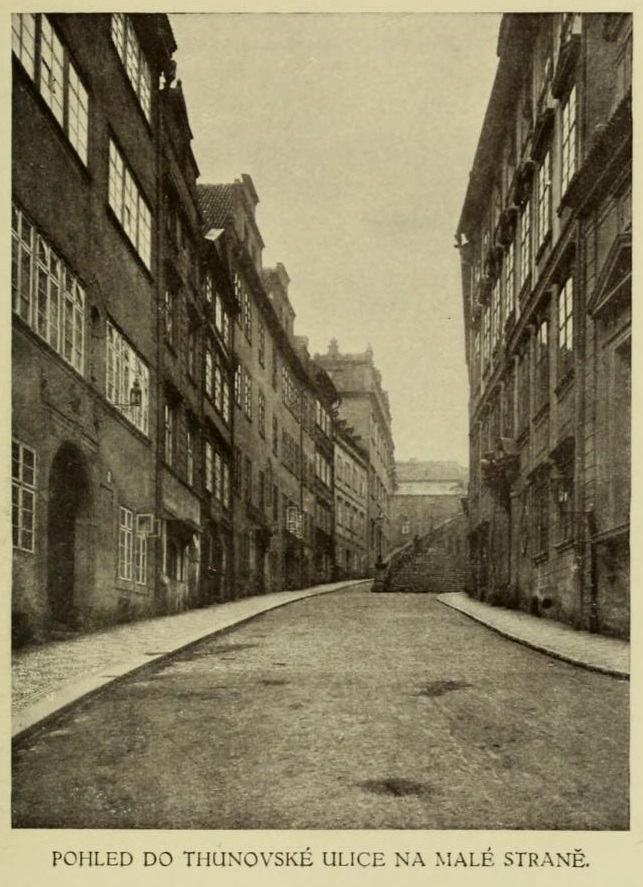 Sepia photograph of a narrow empty street of tall old houses curving uphill towards a flight of steps, no people and no vehicles, captioned in Czech below the image.