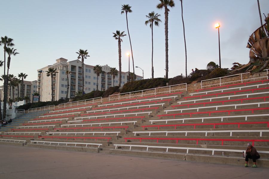Tiered red and white benches of the Junior Seau Pier Amphitheatre in Oceanside under tall palm trees