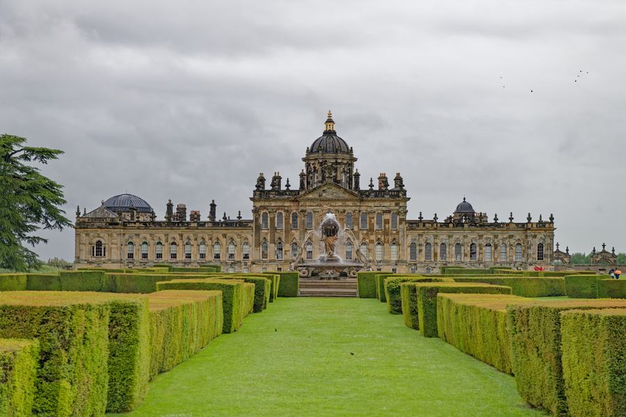 A vast baroque palace with a domed centre block seen down a straight gravel walk between clipped yew hedges and lawns.