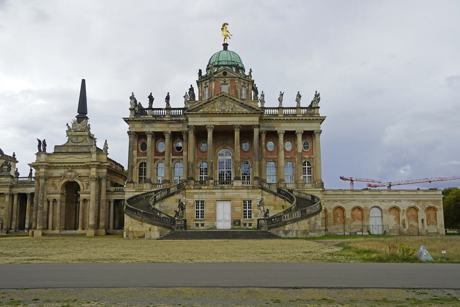 A grand sandstone service building with a domed centre, a columned screen and a double flight of steps, seen across an empty square.