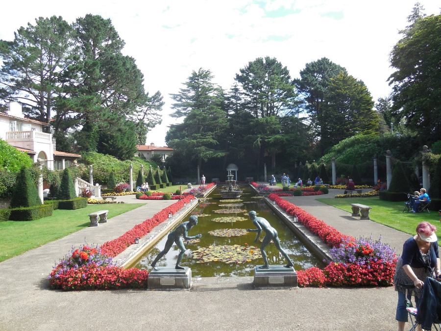 A long formal water canal with fountains, edged by scarlet bedding, low hedges and stone urns, with a loggia at the far end.