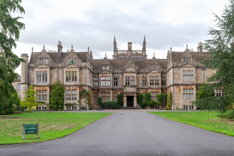 An Elizabethan house of honey-coloured stone with gabled bays and tall mullioned windows, at the end of a curving drive.