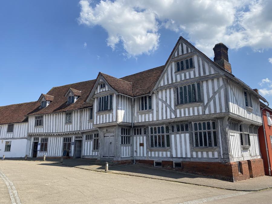 A large timber-framed Tudor building with close-set black beams, white plaster panels, an overhanging upper storey and a tiled roof.
