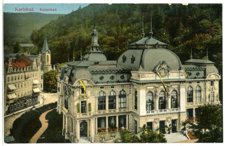 A colour-tinted postcard captioned Karlsbad Kaiserbad, showing the domed spa building from above with a stream and a church spire to the left and a wooded hillside behind.