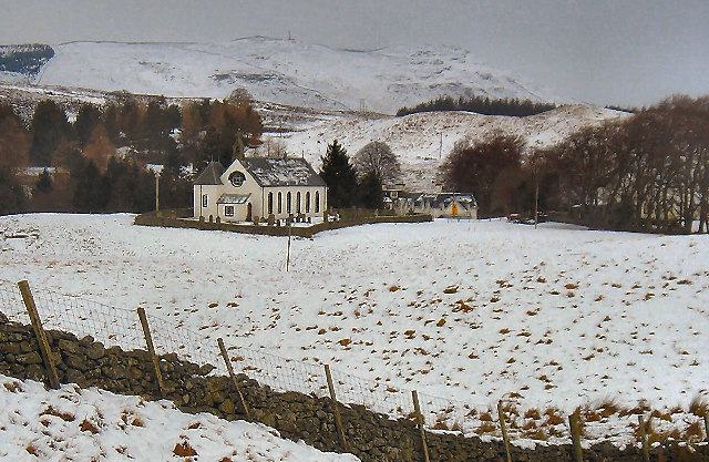 A small white harled church with a bellcote standing alone in a snow-covered valley, with a dry stone wall in the foreground and bare hills behind.