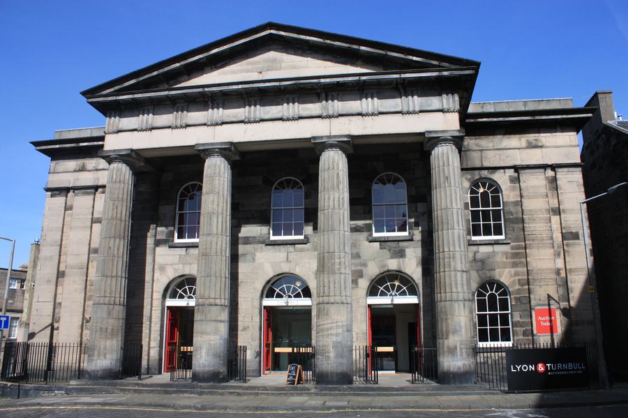 A Greek Revival church front of blond stone with a pediment carried on four heavy Doric columns, red doors, and a small LYON & TURNBULL sign at the corner.