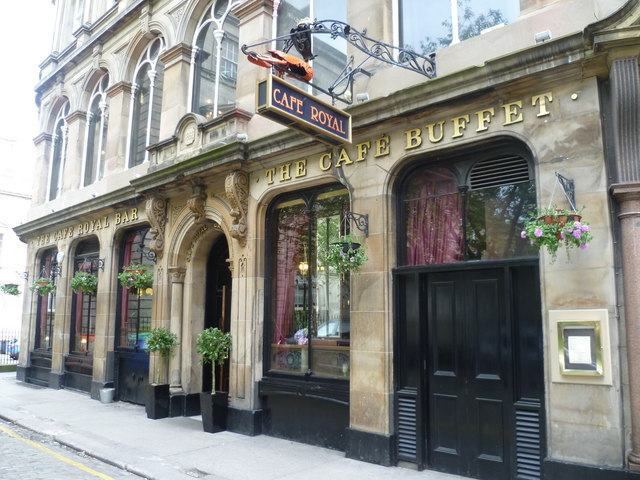 A stone-fronted Victorian corner building with round-headed windows, a wrought-iron hanging sign reading Café Royal, and gilt lettering reading The Café Buffet.