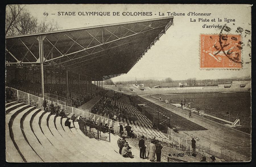 A sepia postcard captioned Stade Olympique de Colombes, showing a long cantilevered grandstand over packed terracing, spectators in the foreground and a cinder track curving away.