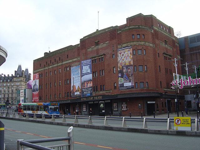 A large brick corner building with rounded edges and stepped massing, posters on the upper walls and ROYAL COURT THEATRE lettered above the ground floor entrance.