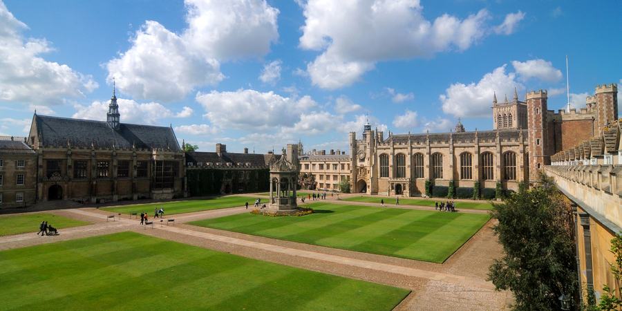 A very large rectangular college court with mown lawns and gravel paths, a stone fountain at the centre, and ranges of Tudor buildings including a chapel and a hall around it.