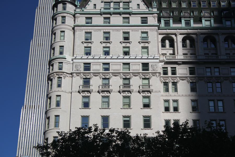 The white stone facade of a large hotel seen from street level, rows of ornamented windows, trees along the pavement below.