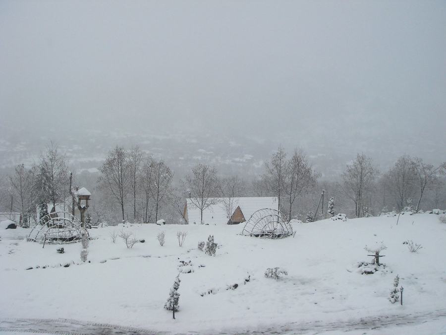Snow-covered gardens and rooftops on a hillside above a town in haze