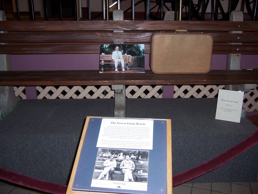 Dark wooden park bench behind a rope barrier in a museum with an explanatory panel