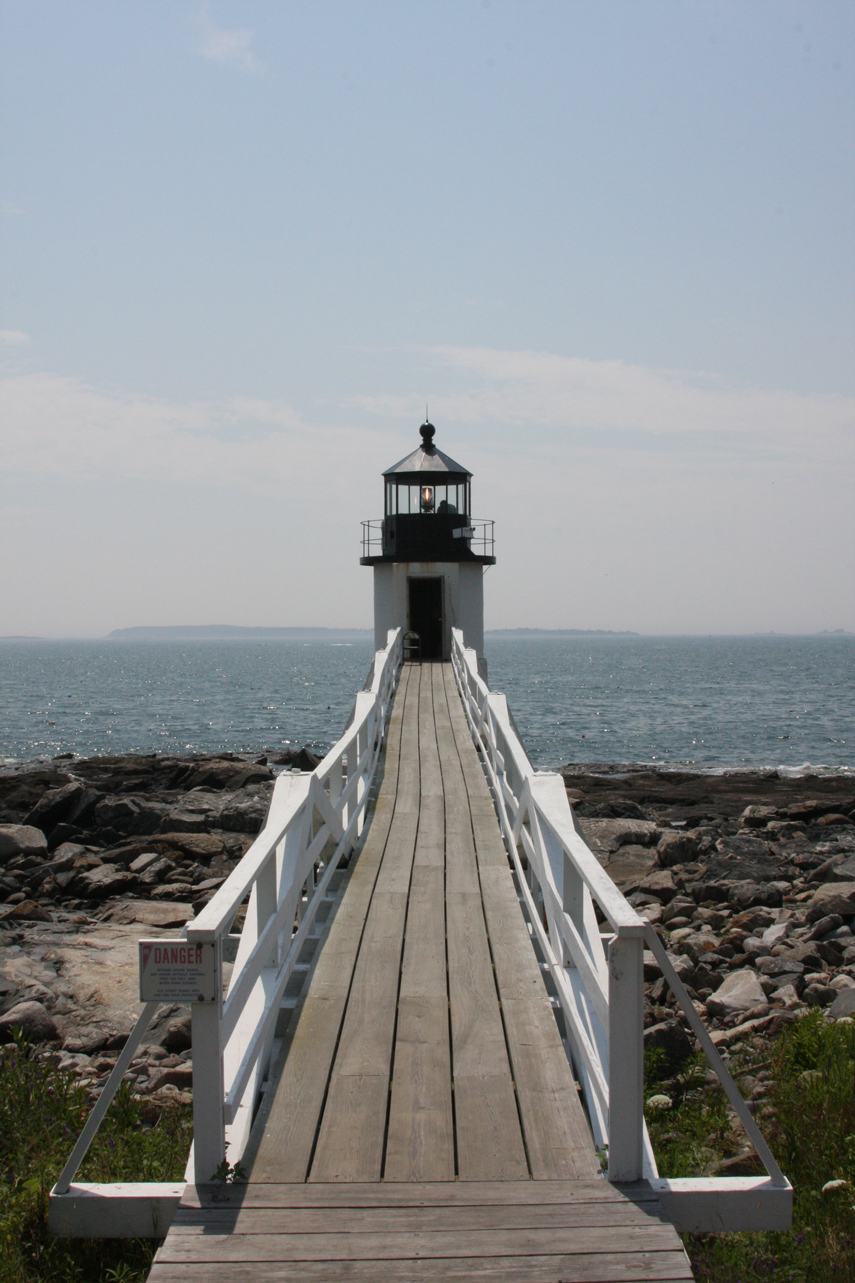 Wooden plank walkway on granite piers leading to a small white lighthouse