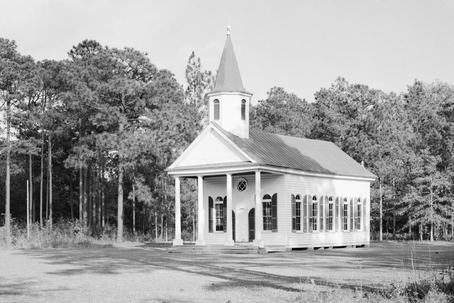 White clapboard chapel with a portico and small spire among pine trees