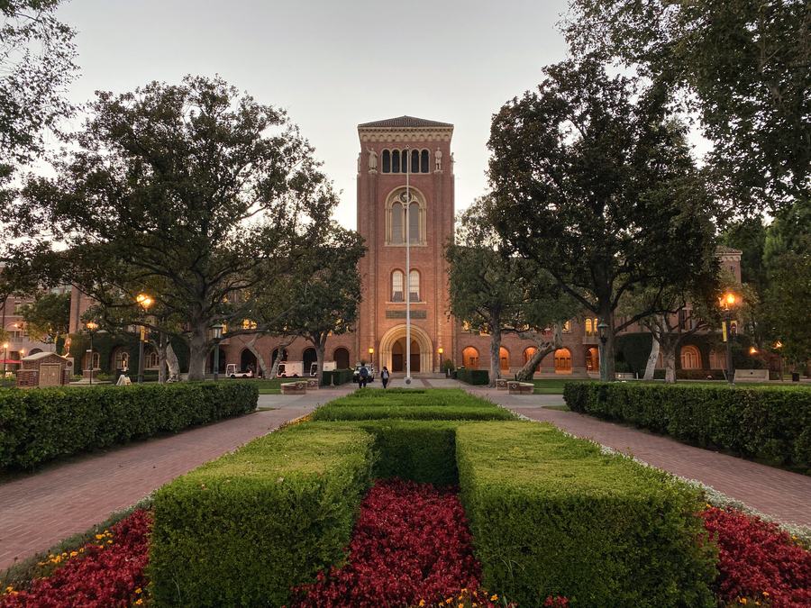 Brick Romanesque building with a tall arched entrance at the end of a formal garden