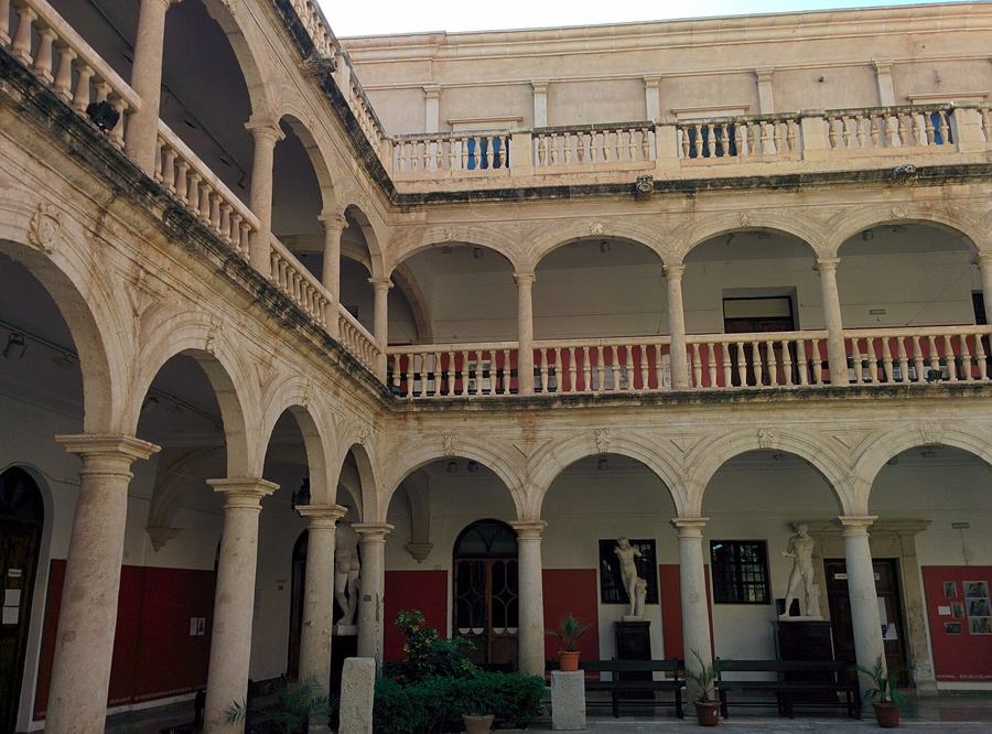 A two-storey arcaded courtyard in pale stone with round arches, balustraded galleries, red painted panels and classical plaster casts on plinths.