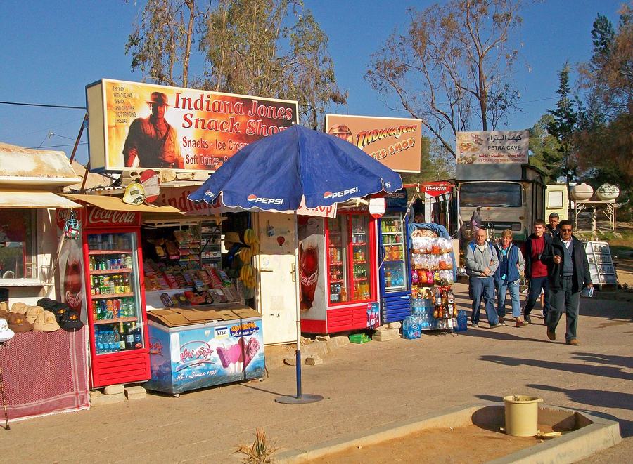 Roadside kiosks selling drinks and souvenirs under signs reading Indiana Jones Snack Shop and Indiana Jones Gifts Shop, with a painted figure in a fedora.