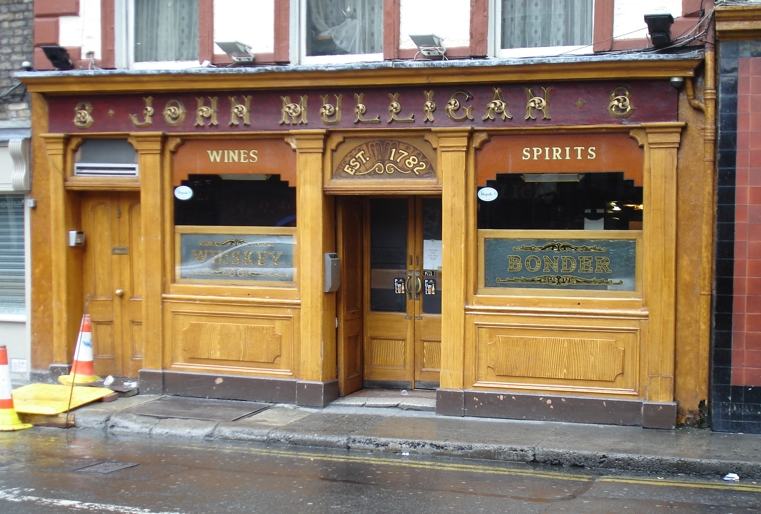 The wooden Victorian shopfront of John Mulligan's pub on Poolbeg Street, Dublin: gold lettering on a dark red fascia reading JOHN MULLIGAN, the words WINES and SPIRITS on either side, EST. 1782 over the central door, and two gilded glass panels reading WHISKEY and BONDER.