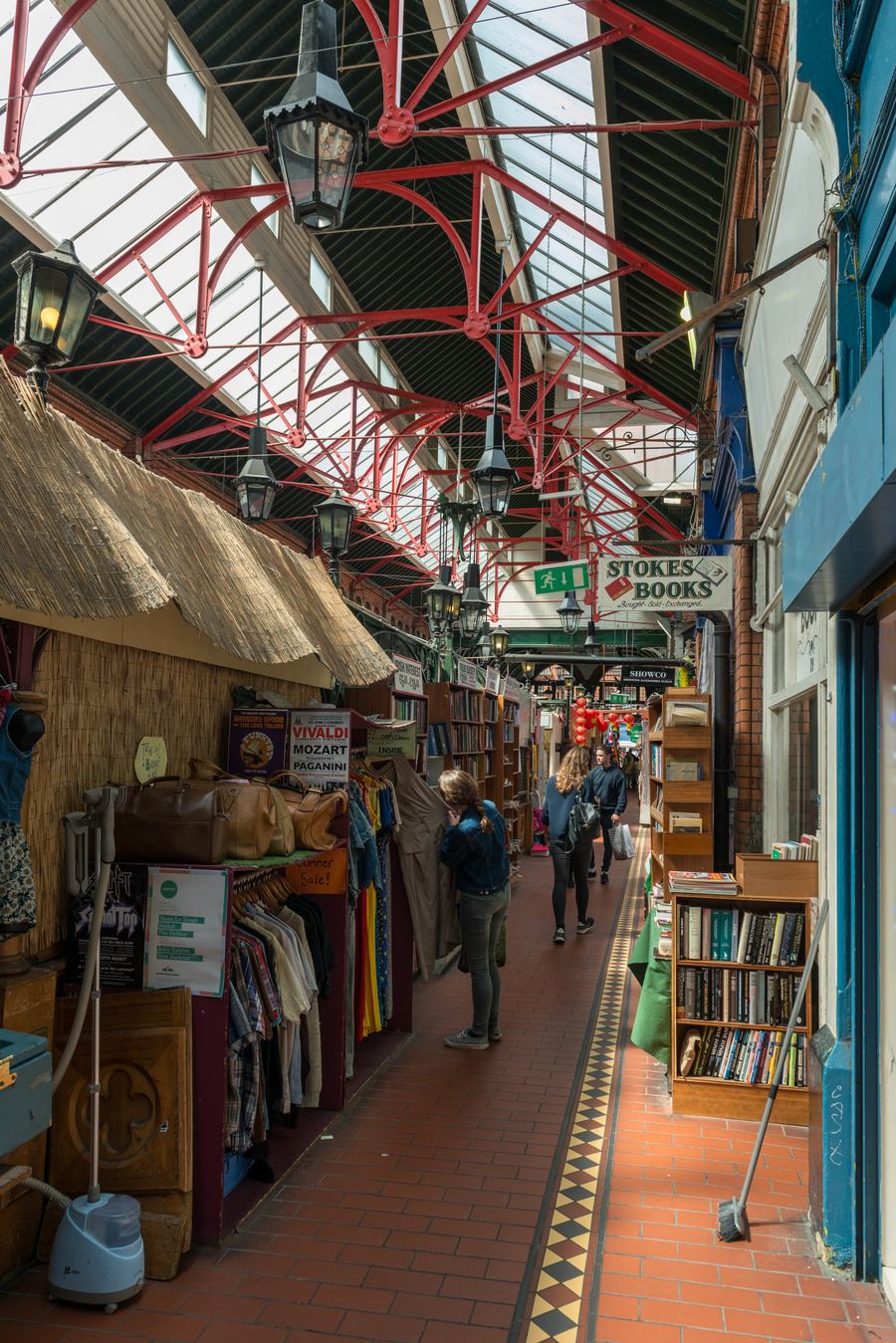 The interior of George's Street Arcade in Dublin: a covered aisle of stalls and small shops under a red painted iron and glass roof.