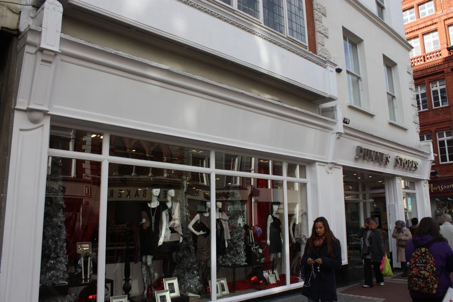 The Dunnes Stores shopfront on Grafton Street, Dublin, with lit window displays and shoppers on the pavement in front of it.