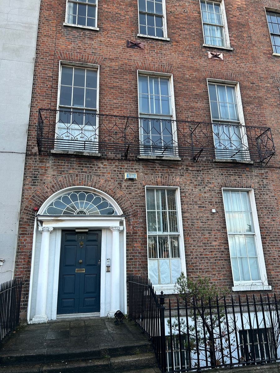 A brick building on Mountjoy Square East, Dublin, with metal fire escapes, steel framed windows and a Georgian doorcase with a fanlight over the door.