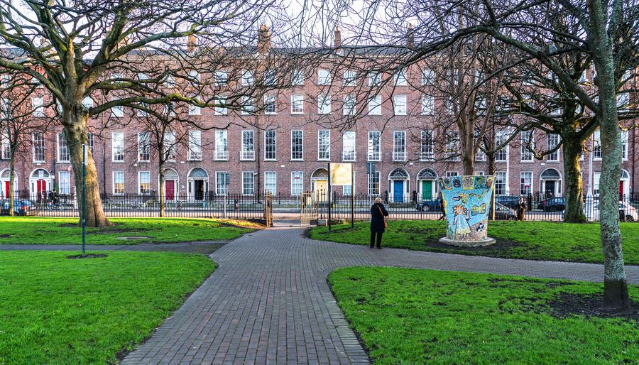 Georgian townhouses along one side of Mountjoy Square in Dublin, seen across the grass and paths of Mountjoy Square Park.