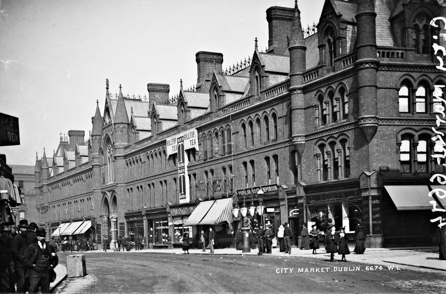 Black and white photograph from about 1895 of the South City Markets building on South Great George's Street, Dublin, with awnings out and people standing on the pavement.