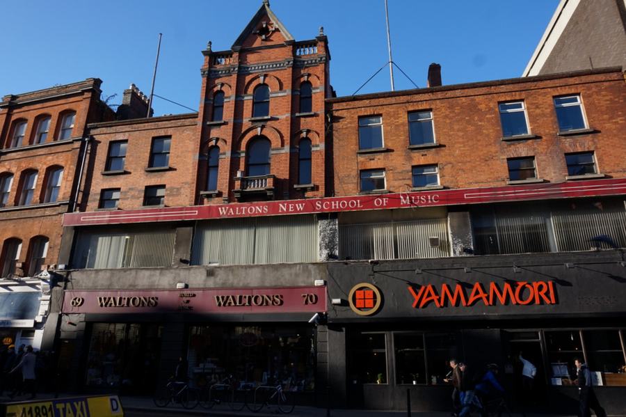A red brick building on South Great George's Street, Dublin, with WALTONS NEW SCHOOL OF MUSIC lettered across the first floor and the shopfronts numbered 69 and 70 at street level.