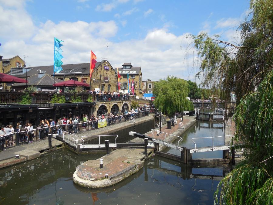 Camden Lock on a summer day: crowds on the terraces of the market buildings above the towpath, the lock gates in the foreground.