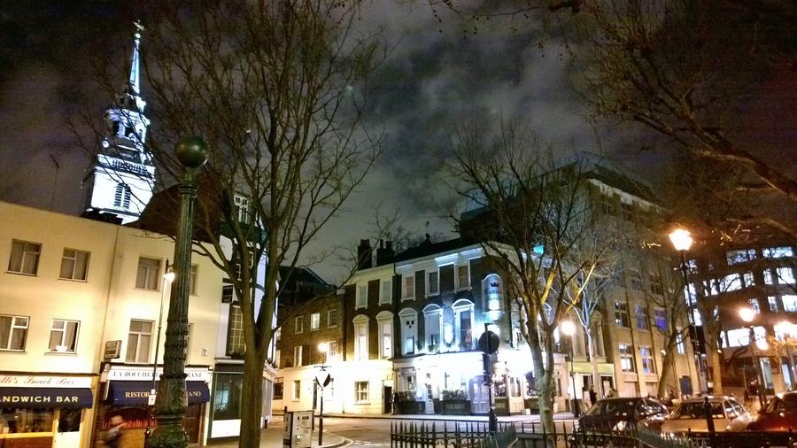 Clerkenwell Green at night, the lit front of the Crown Tavern on the left and the spire of St James's Church behind.
