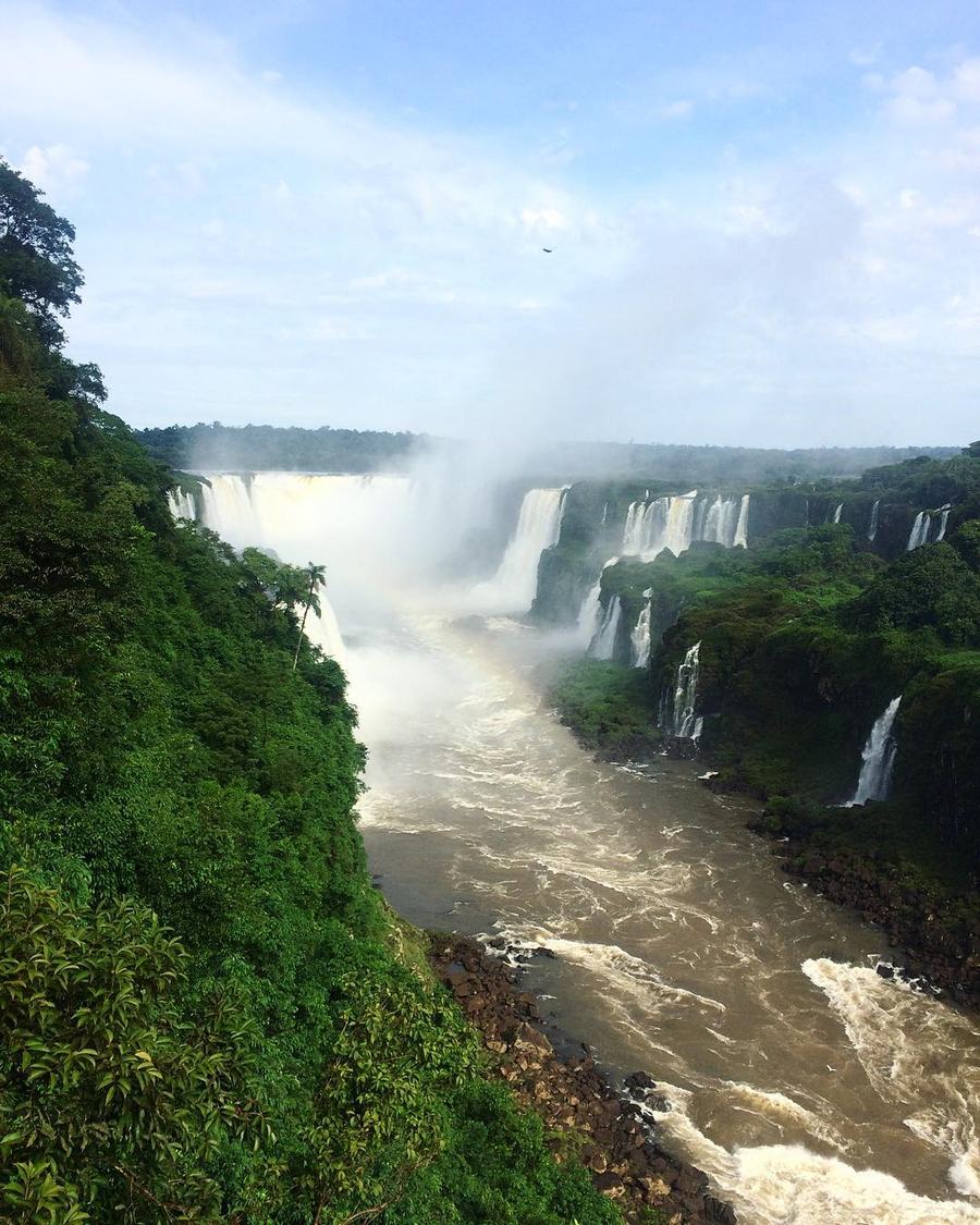 Iguazu Falls seen from a distance from the Brazilian side, several falls dropping over a forested escarpment into the river below.