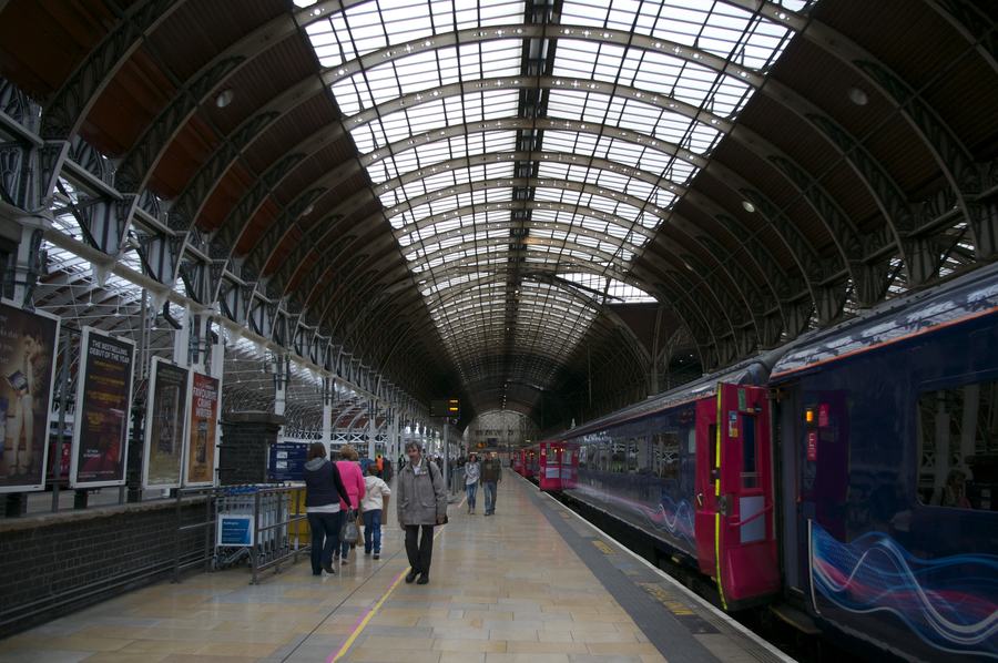 Inside Brunel's train shed at London Paddington: the three glazed arched spans, trains at the platforms and passengers walking towards the camera.