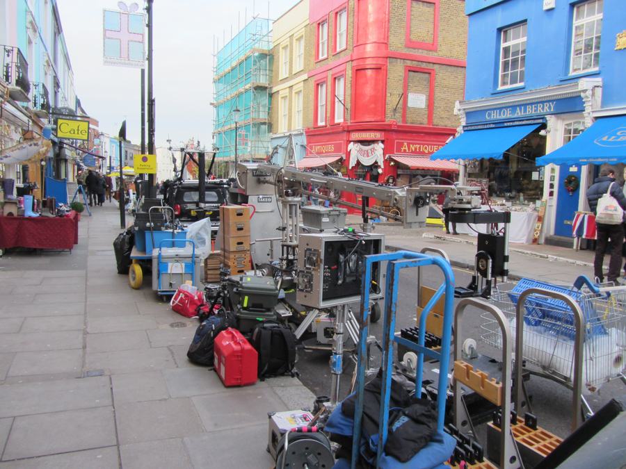 Film equipment — dolly, flight cases, lamps and stands — parked along the pavement of Portobello Road in front of the painted shopfronts, during the shooting of Paddington on 26 November 2013.