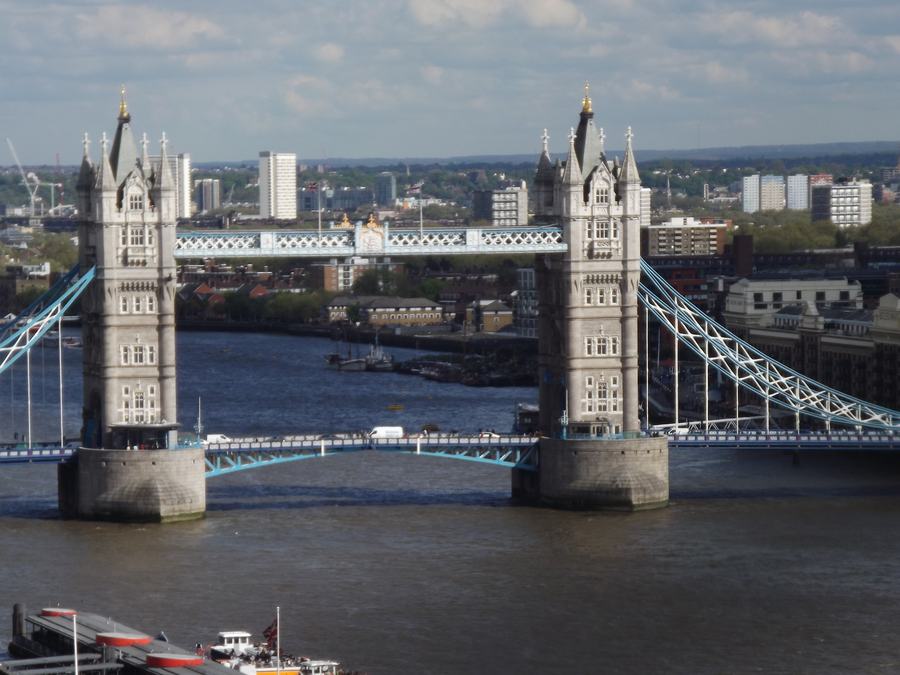 Tower Bridge from above and upstream, both towers and the suspended side spans, the Thames below and east London behind.