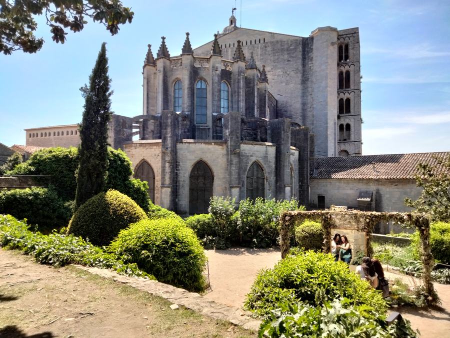 A terraced garden of box hedges inside the old city wall, the buttressed east end of a Gothic cathedral and a Romanesque tower behind.