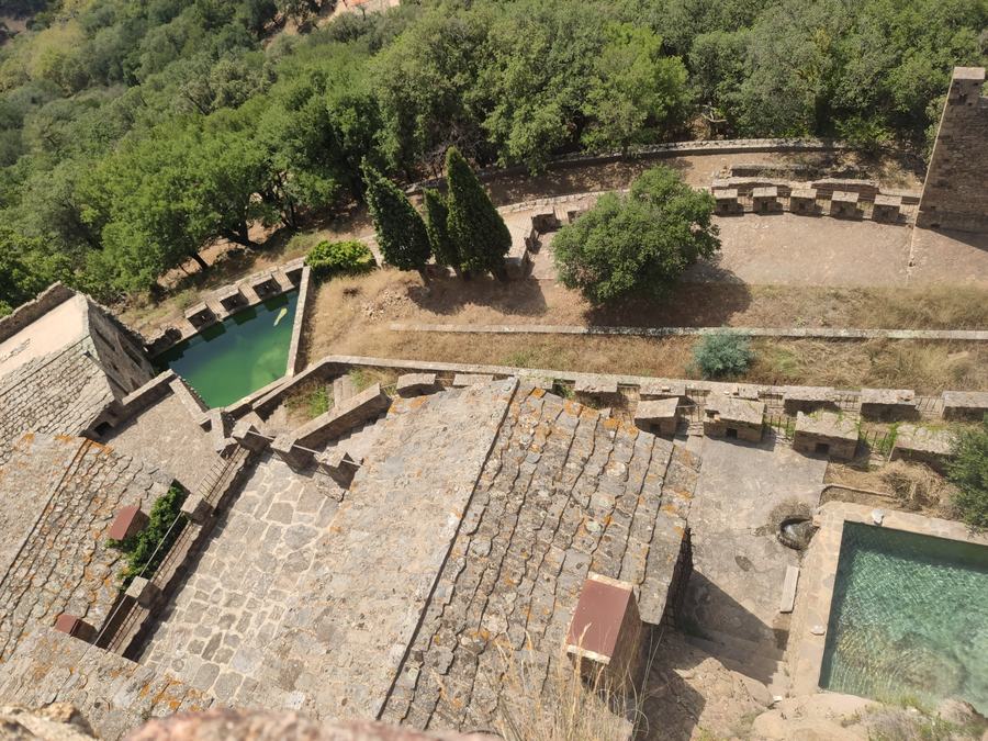 Looking down on terraces, crenellated walls, two green water tanks and oak woodland beyond.