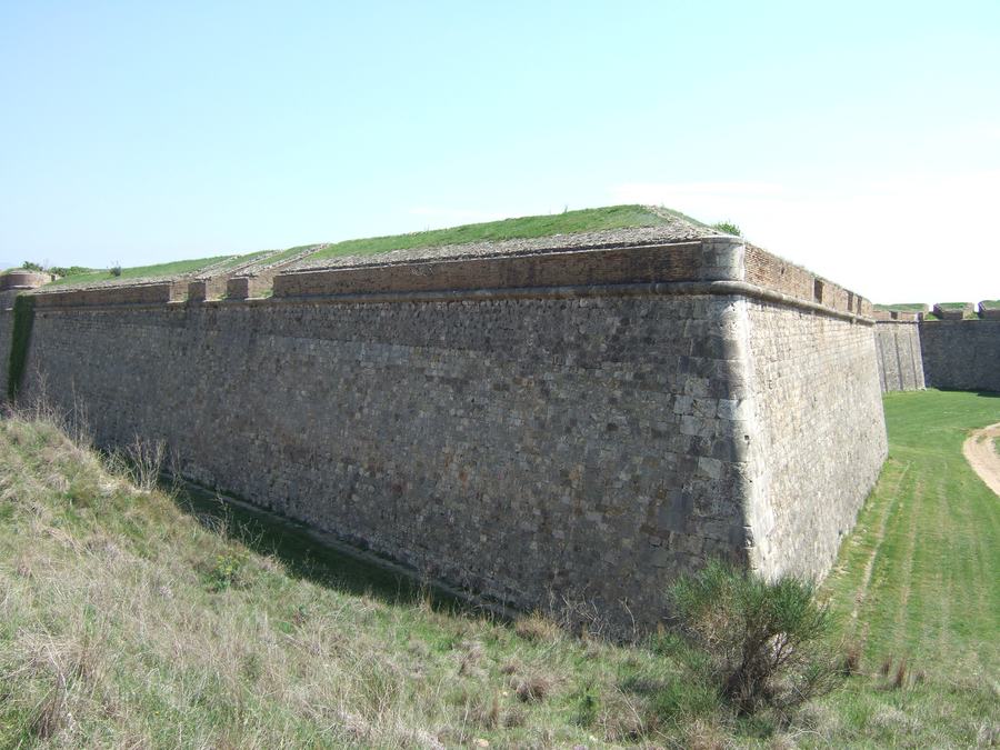 A long angled masonry rampart with a grassed top, falling to a deep dry ditch.