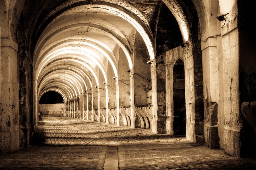 A long brick-vaulted hall on square piers, receding arches, cobbled floor, warm-toned photograph.