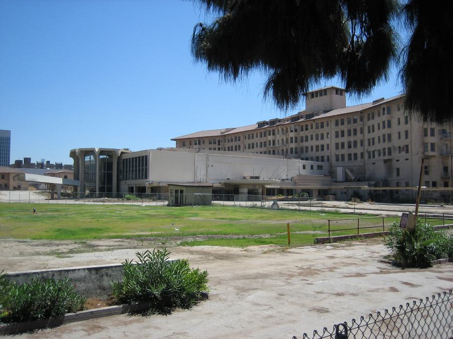 Long derelict hotel building behind a chain link fence and an empty lot
