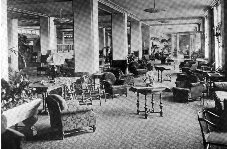 Long hotel lobby with columns, wicker chairs, potted palms and patterned carpet