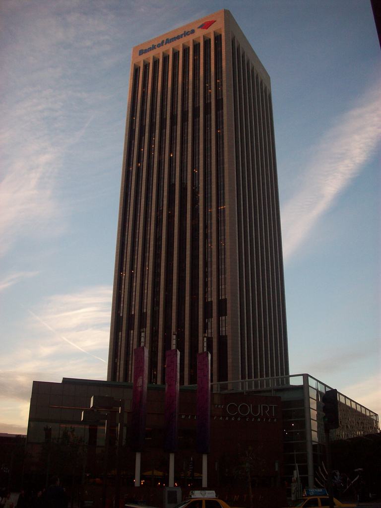 Tall dark office tower at dusk with banners and a low plaza building in front