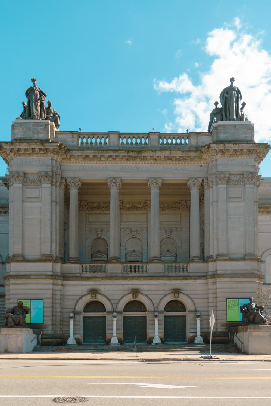Grand stone facade with a colonnade, balustrade and seated statues on the roofline