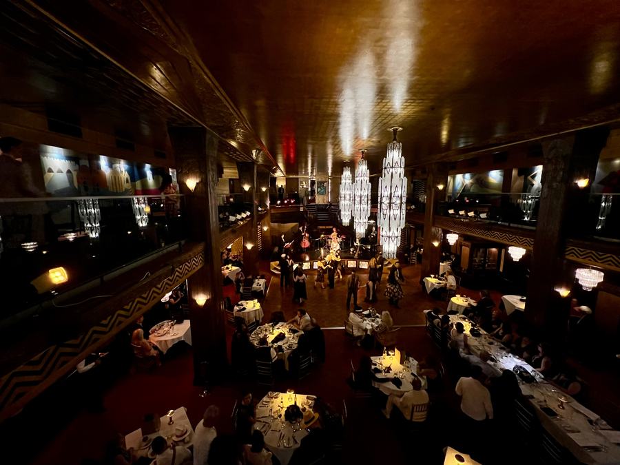 Dark art deco double-height room with chandeliers, balconies and set tables