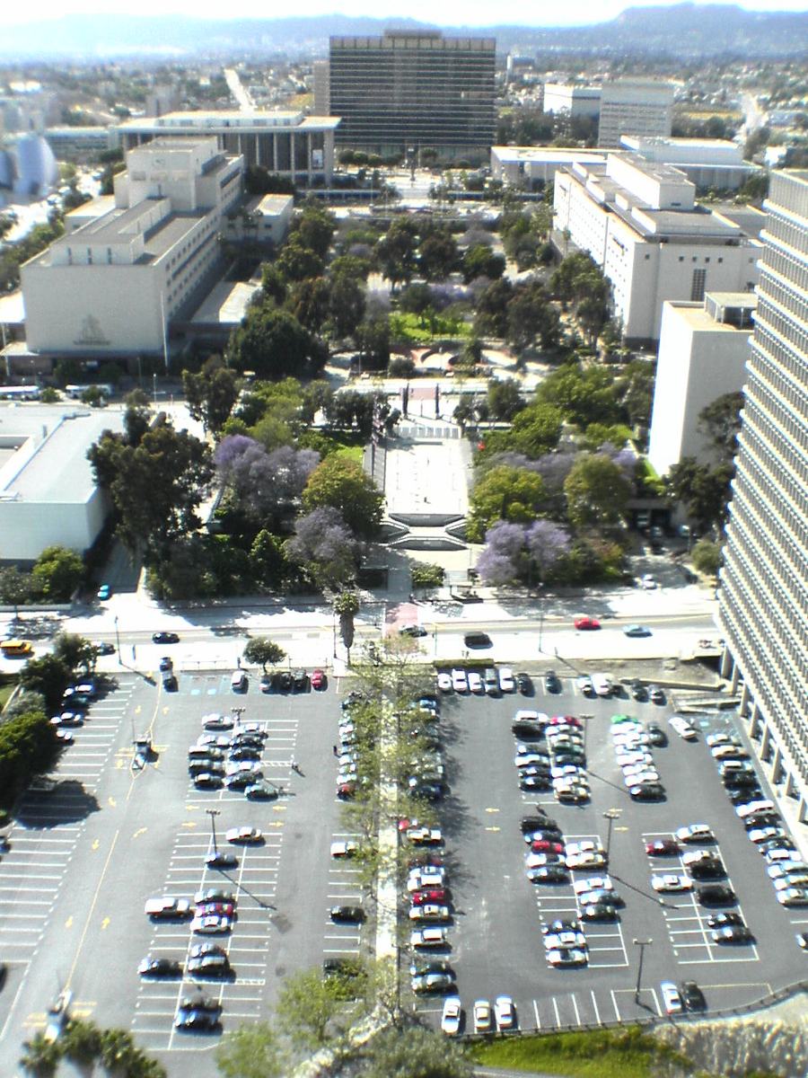 Aerial view of a narrow strip of park between civic buildings and a large car park