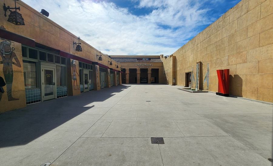 Long open courtyard with painted Egyptian columns and shopfronts leading to a cinema entrance