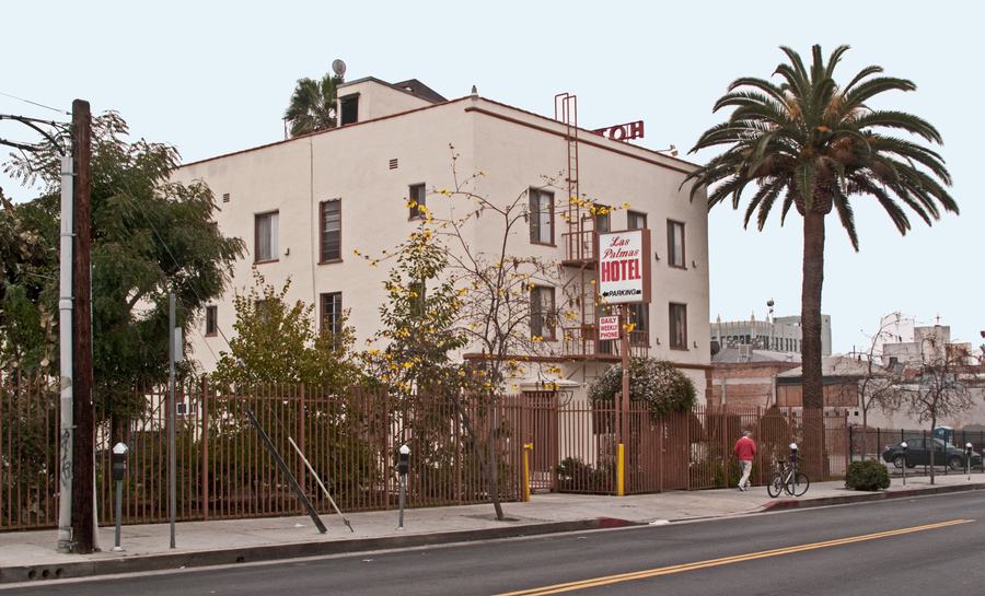 Three-storey cream stucco hotel on a corner with a red vertical HOTEL sign and an iron fire escape