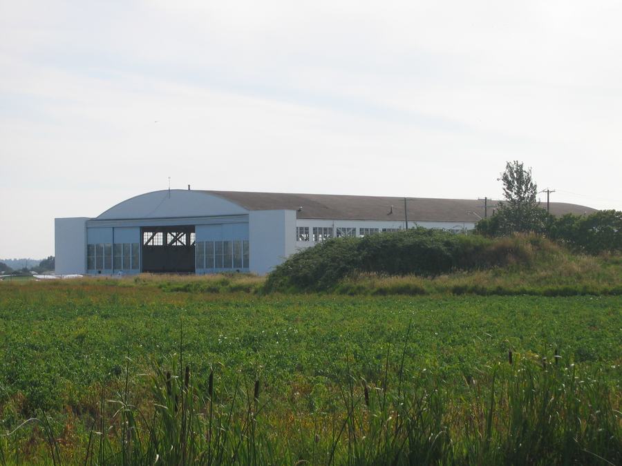 Large curved-roof aircraft hangar with an open door seen across a green field