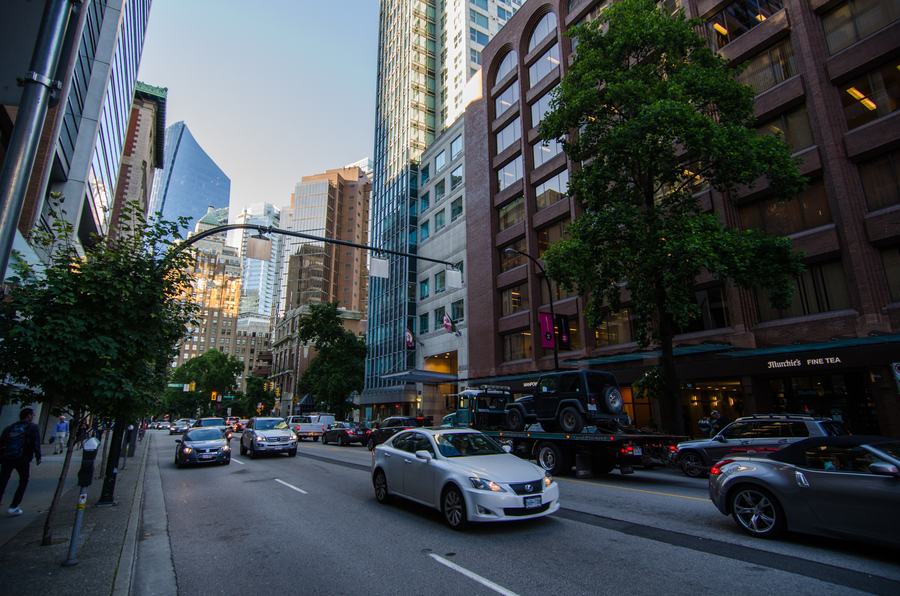 Downtown street lined with office towers and a brick building, traffic in both directions in evening light