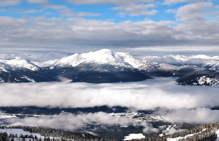 Snow-covered mountain massif rising above a layer of cloud filling a valley, seen from a ski slope, winter